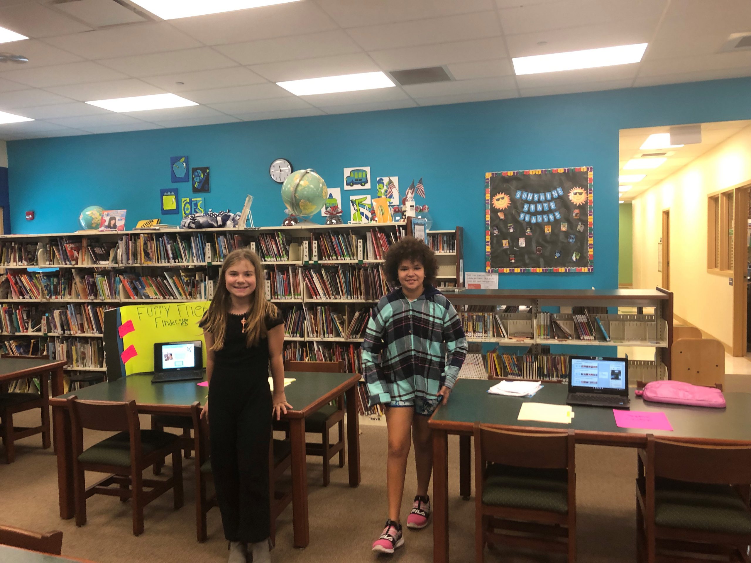 Two students standing near tables in the media center.